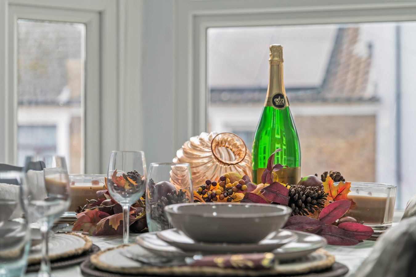 A table set for a meal with a bottle of champagne, glasses, and a decorative centerpiece.
