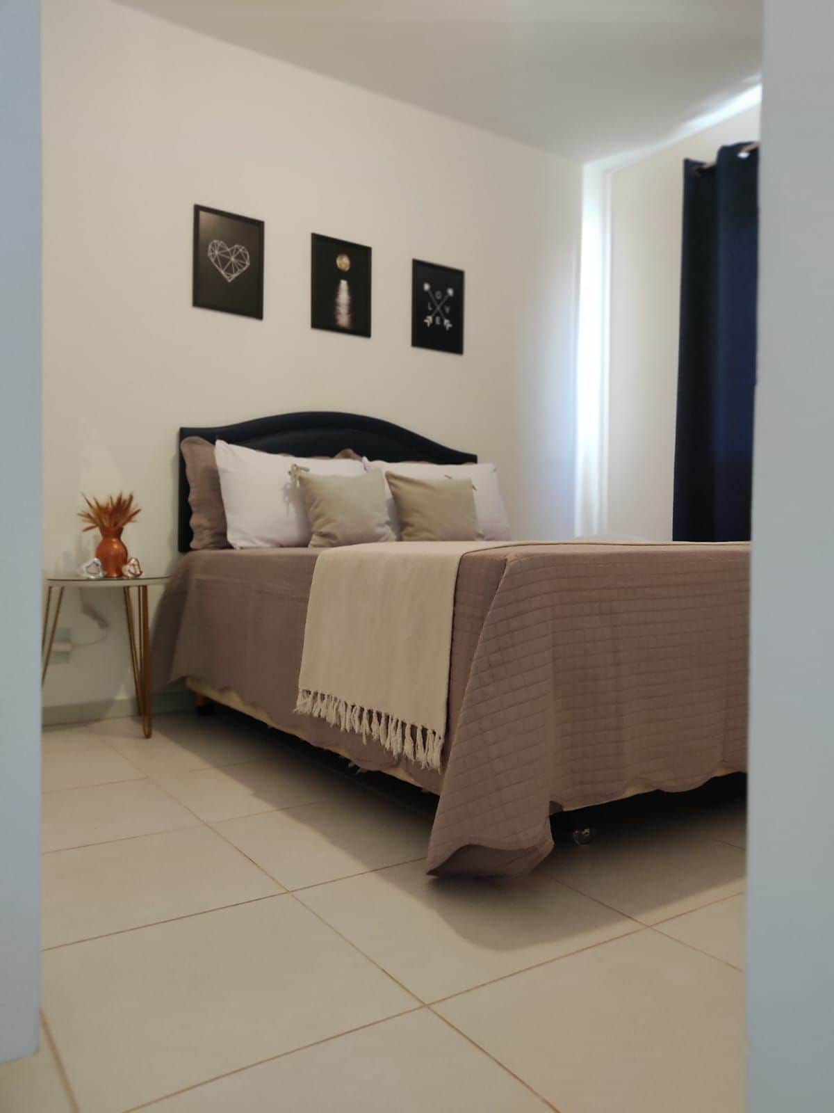 A bedroom with a bed, a bedside table, and a wall with three framed pictures.