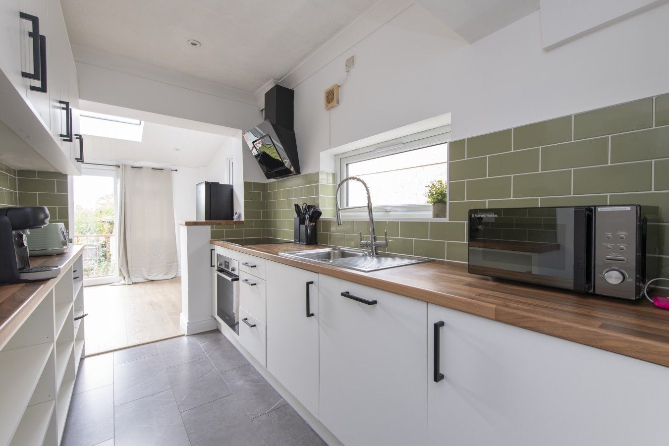 Una cocina moderna con armarios blancos, encimera de madera, microondas integrado y ventana sobre el fregadero.