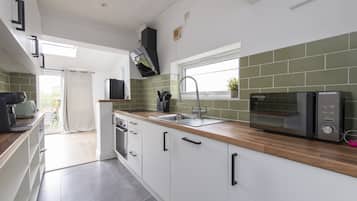 Una cocina moderna con armarios blancos, encimera de madera, microondas integrado y ventana sobre el fregadero.