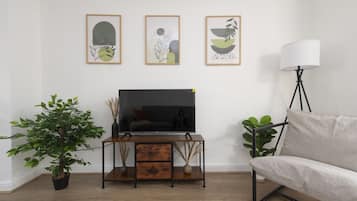 Una sala de estar con un televisor sobre un soporte de madera, un sofá, una lámpara de pie y tres cuadros en la pared.