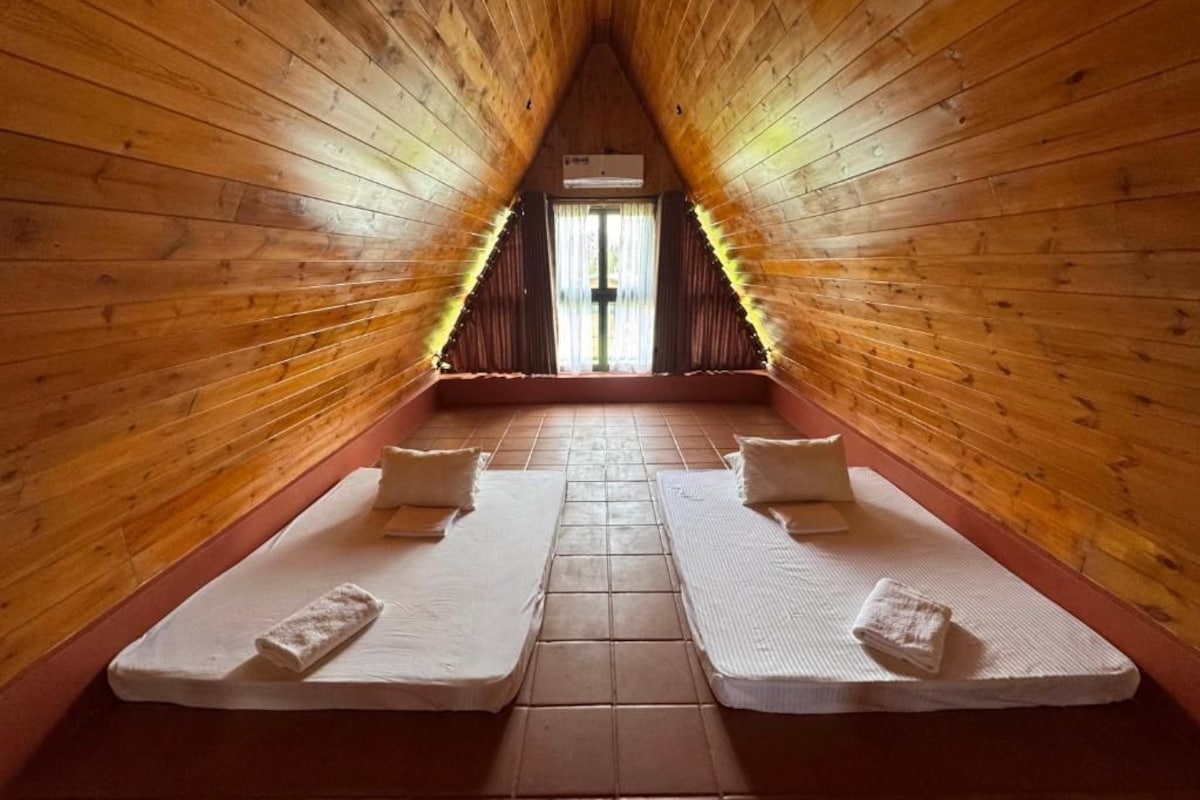 A room with a sloped ceiling and wooden walls, featuring two beds with pillows and towels.