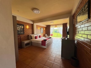 A hotel room with a bed, a small table, a TV, and a balcony with a view. - Ahas Pokuna Holiday Resort (Barandana)