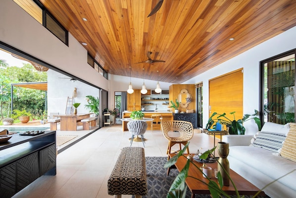 Un interior modern amb sostre de fusta, zona de menjador, cuina i saló amb sofà i plantes.