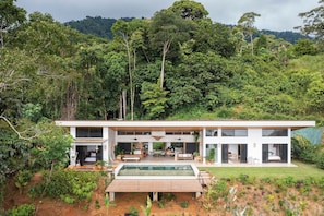 A modern two-story house with a large glass facade, a swimming pool, and a lush garden. - Hidden Villa Oasis: Infinity Pool & Ocean Views near Dominical (Savegre de Aguirre)