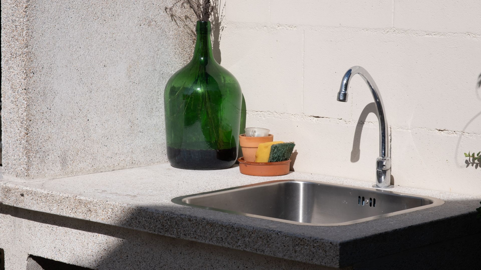 Un évier de cuisine avec une bouteille verte, une éponge et un petit récipient.