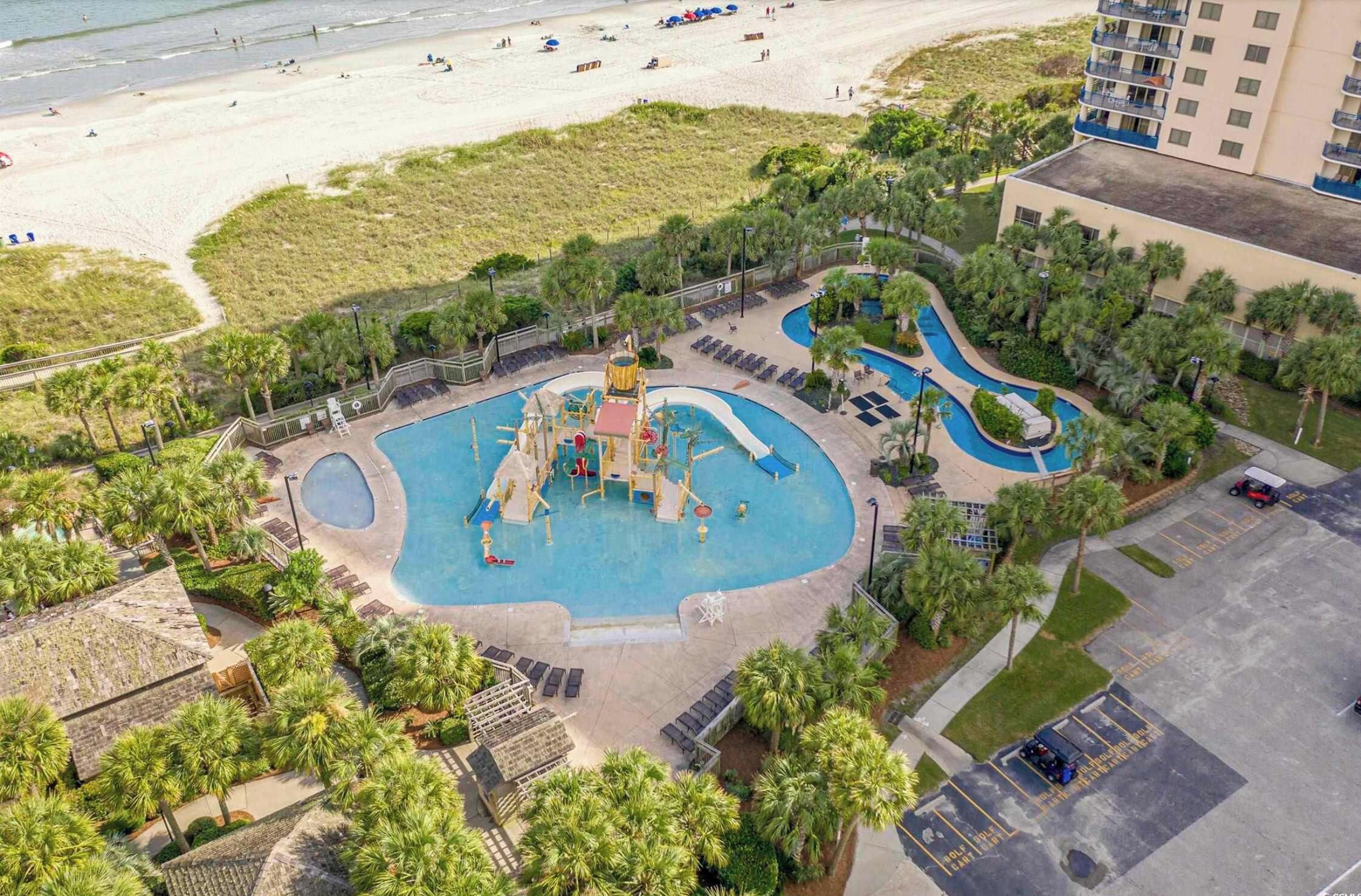 A resort with a central pool area, a beach, and a parking lot.