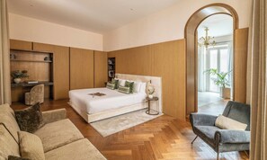 A modern bedroom with a large bed, a sitting area with a sofa and armchair, wooden paneling, and a view of the outdoors through an arched window. - REFINED 3-BEDROOM PALAZZO STAY NEAR CAMPO DE’ FIORI AND PIAZZA NAVONA (Roma)