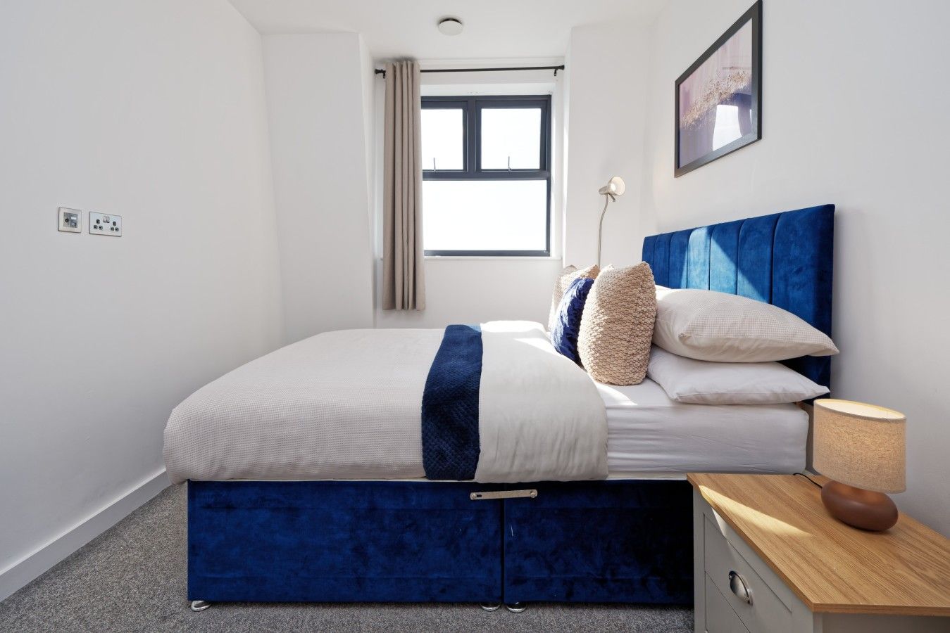 A bedroom with a bed, bedside table, lamp, and a window.