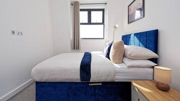 A bedroom with a bed, bedside table, lamp, and a window.