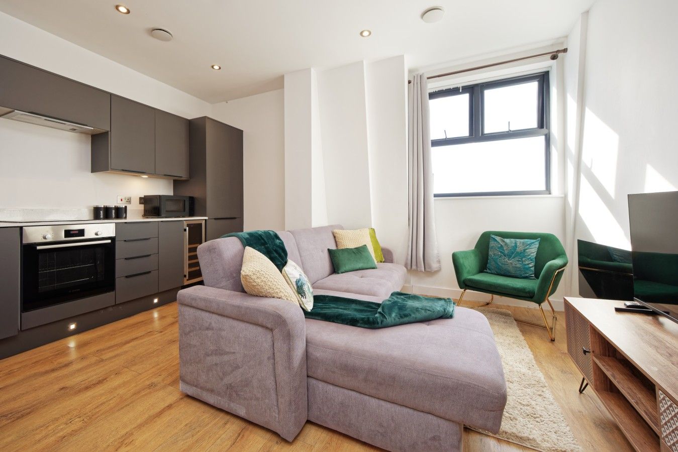 Ein modernes Wohnzimmer mit einem grauen Sofa, einem grünen Sessel und einem Flachbildfernseher.