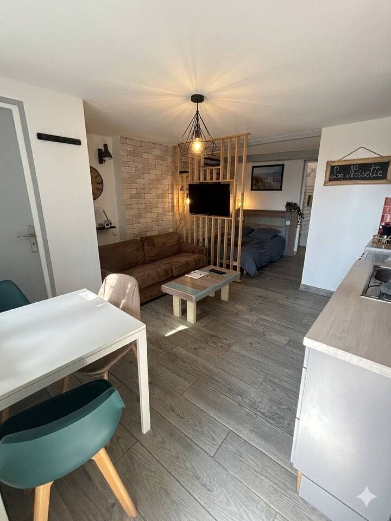 Een knus woongedeelte met een bank, een salontafel, een aan een houten wand bevestigde televisie, en een klein kitchenette.