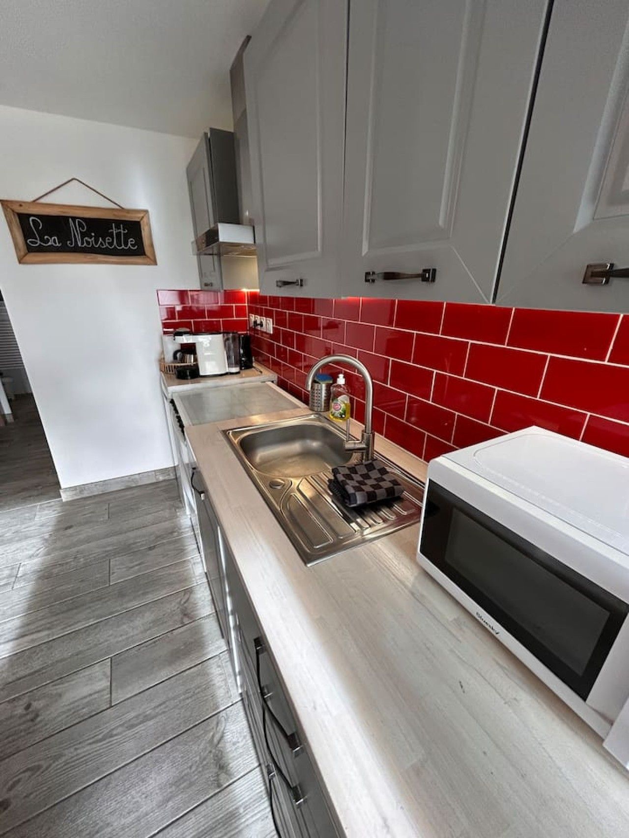 Een moderne keuken met een spoelbak van roestvrij staal, een magnetron en een rode tegelwand.