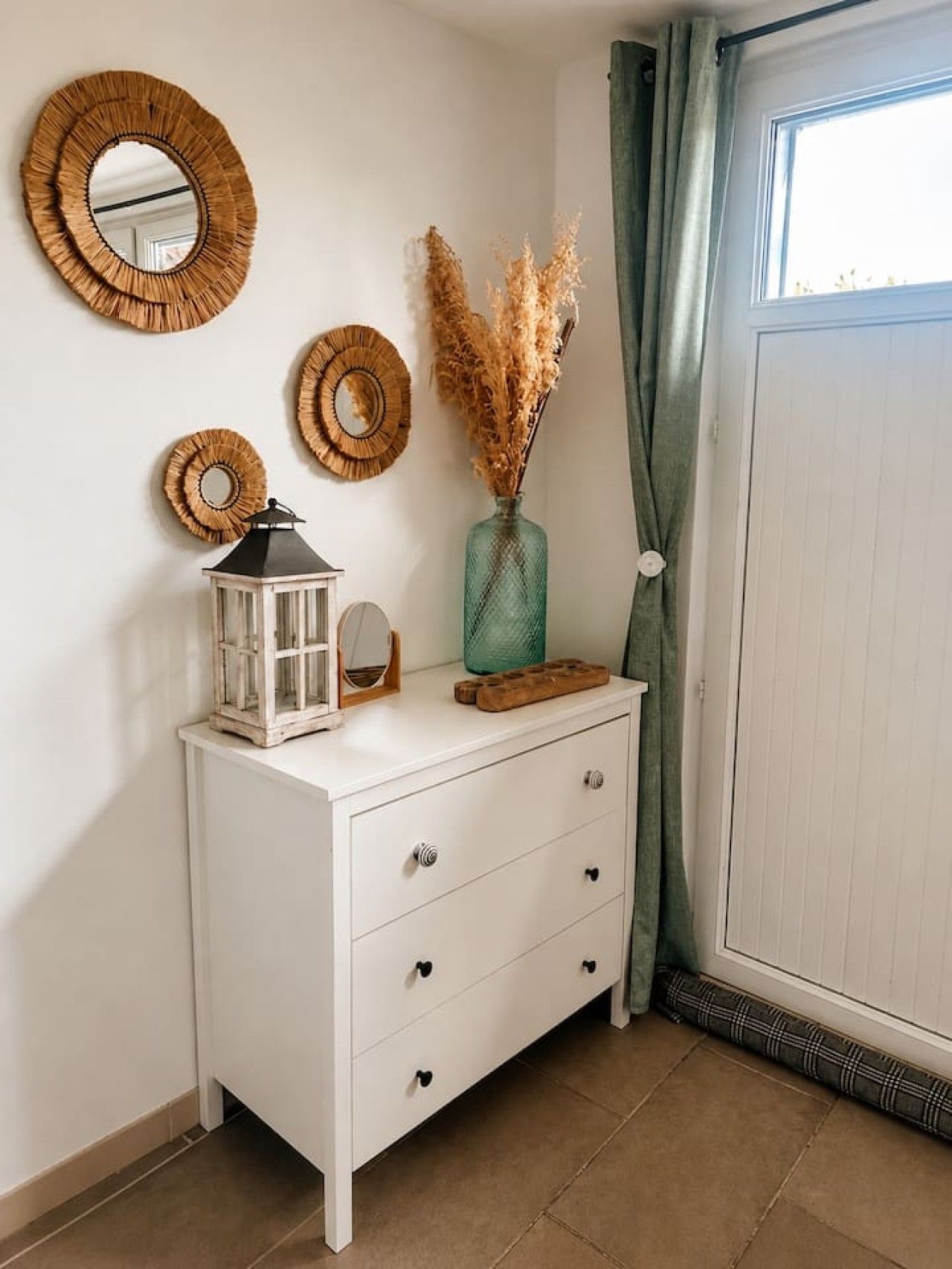 A white dresser with three drawers, a lantern, and decorative mirrors on the wall.
