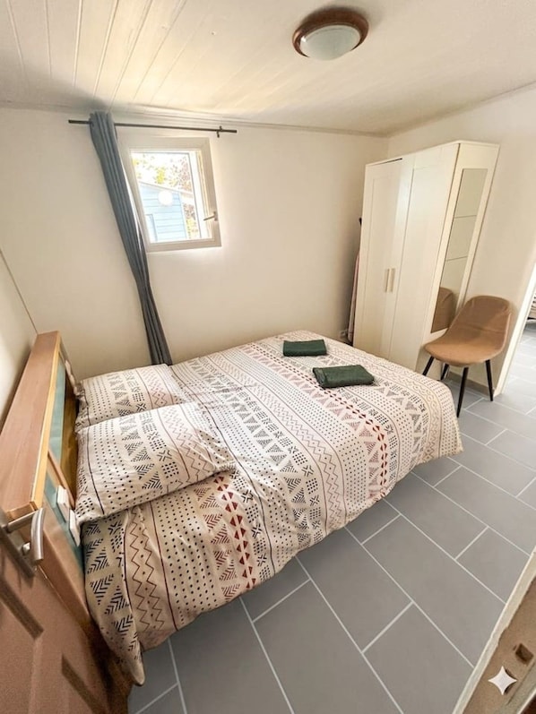 Et soveværelse med seng, garderobeskab, stol og et vindue.