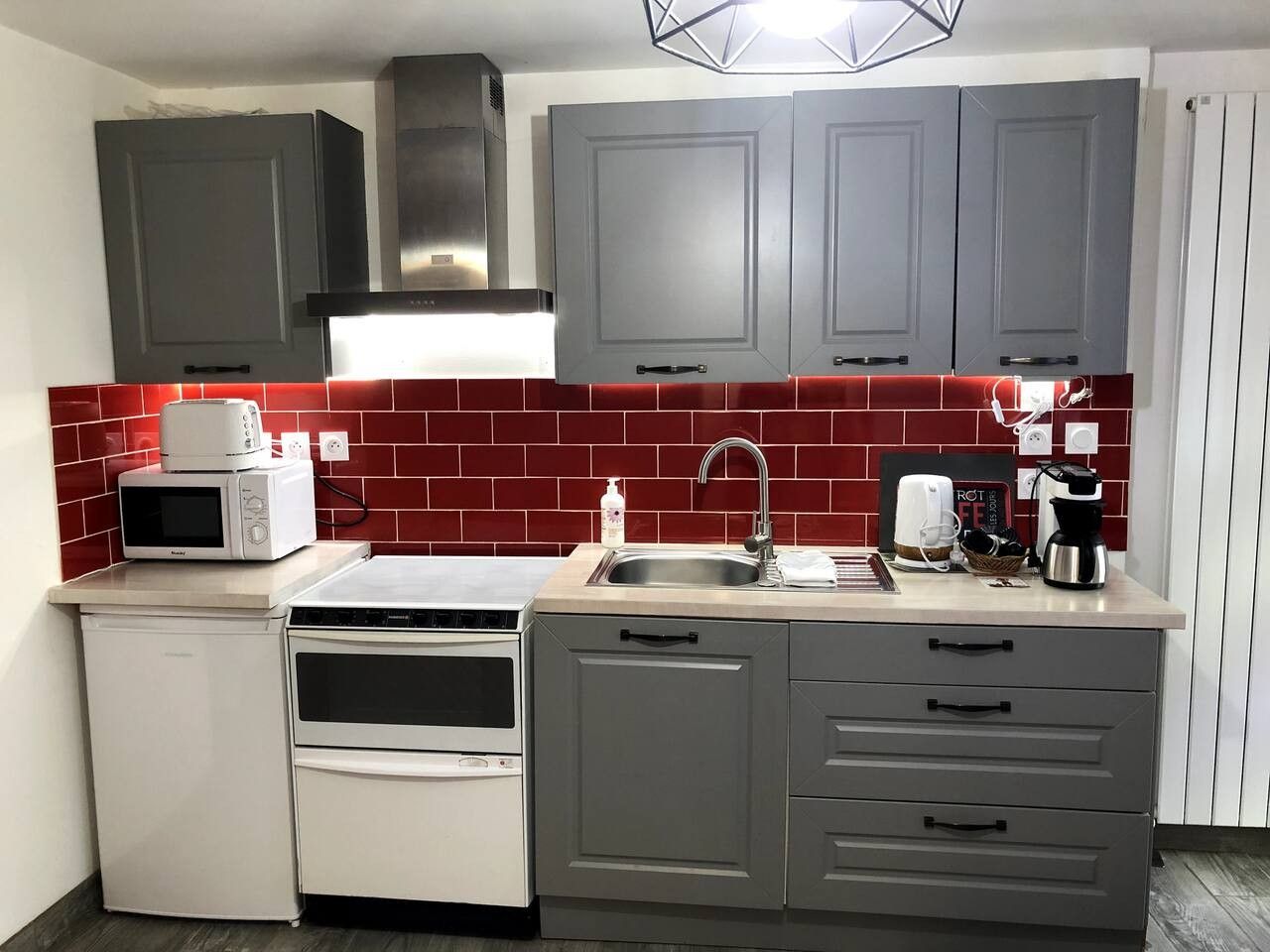 A compact kitchen with grey cabinets, a microwave, a toaster, a coffee maker, and a sink.