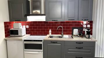 A compact kitchen with grey cabinets, a microwave, a toaster, a coffee maker, and a sink.