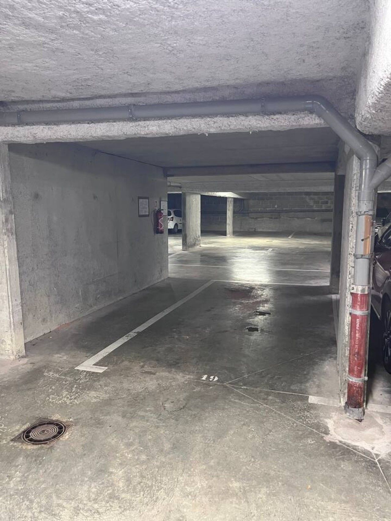 An underground parking garage with concrete walls, a wet floor, and a fire extinguisher mounted on the wall.