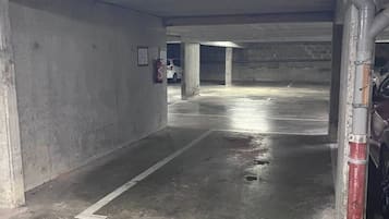 An underground parking garage with concrete walls, a wet floor, and a fire extinguisher mounted on the wall.