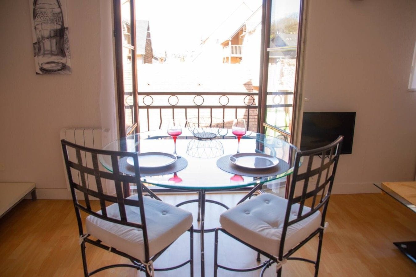 A dining area with a glass table and metal chairs, two wine glasses, and a view of buildings through a window.