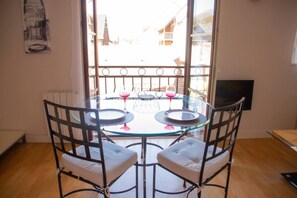 Comedor con mesa de vidrio, sillas de metal, dos copas de vino y vista a edificios a través de una ventana.