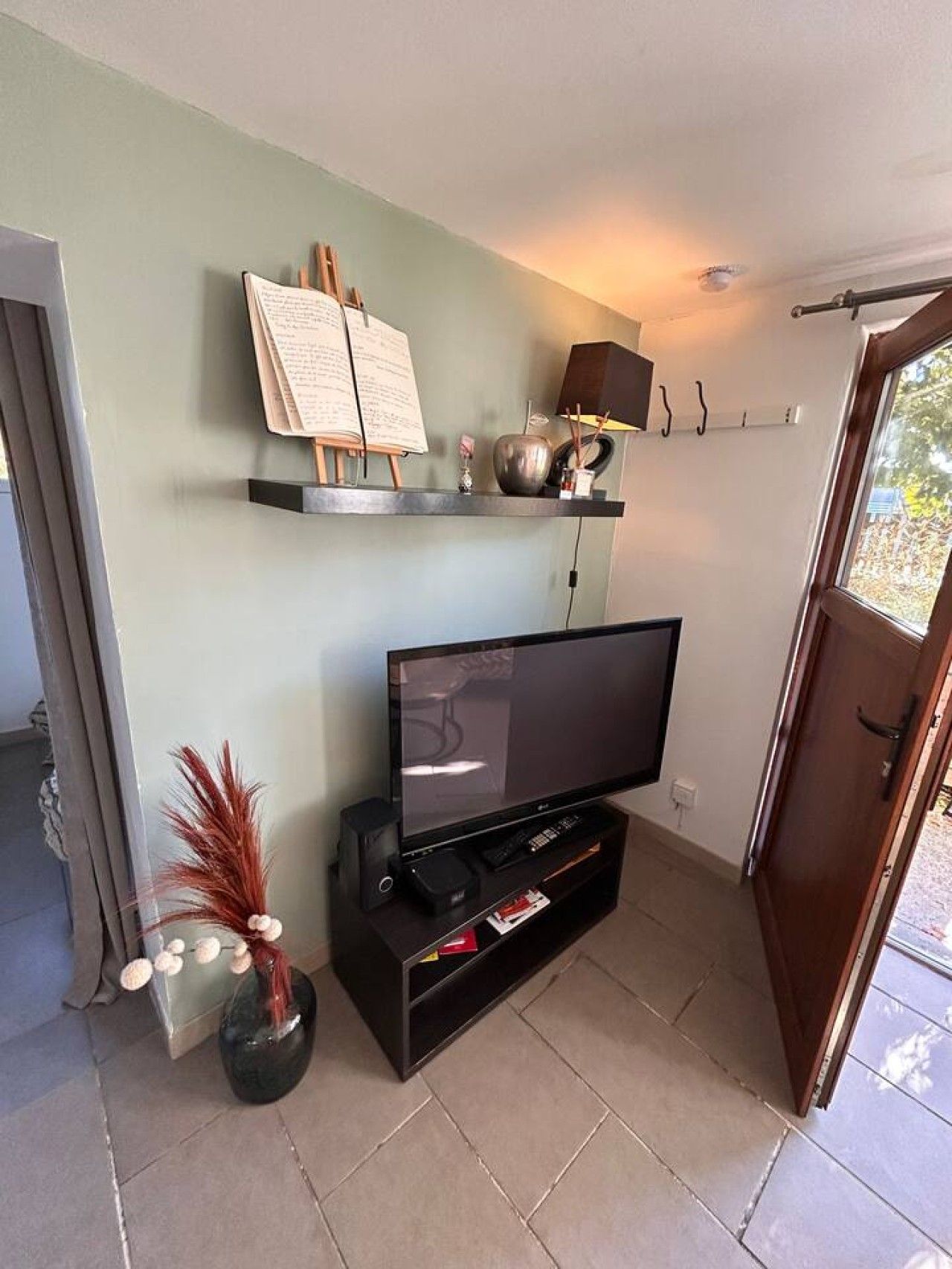 A living room with a flat-screen TV on a stand, a music stand with sheet music, a lamp, and a decorative vase.