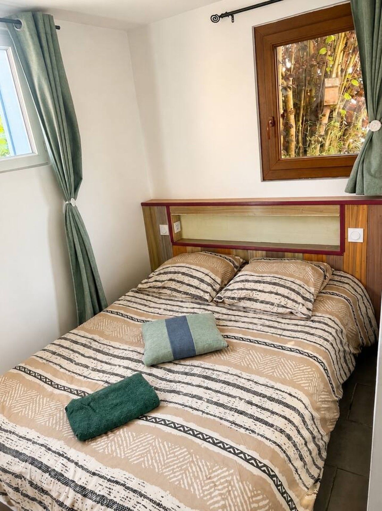 A bed with patterned bedding and pillows, a window with curtains, and a mirror on the wall.