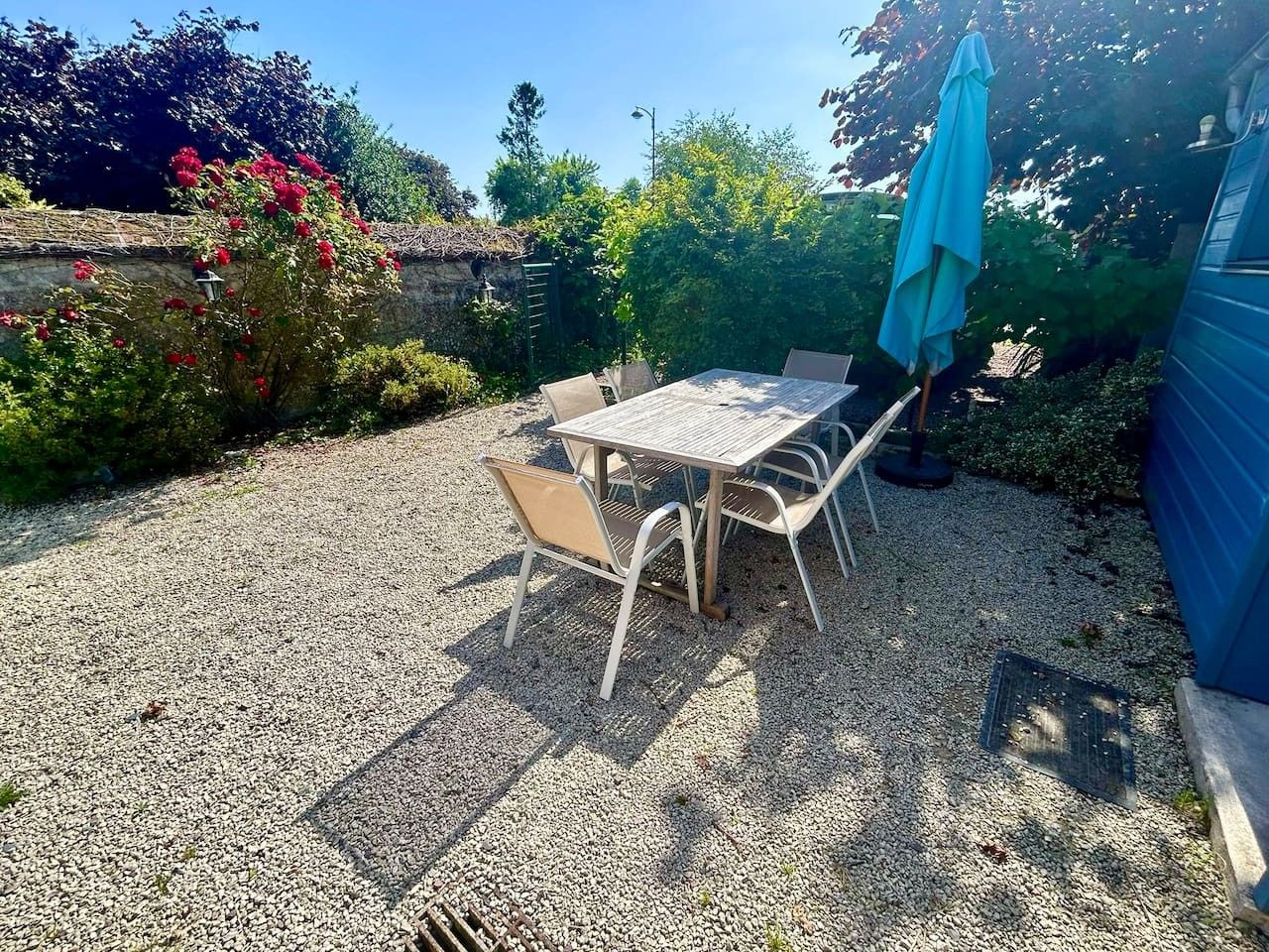 An outdoor patio with a table and chairs, surrounded by gravel and greenery.