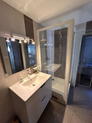 Un baño moderno con un espejo grande, un lavamanos y un box de ducha.