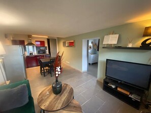 Ein modernes Wohnzimmer mit Flachbildfernseher, Essbereich mit Tisch und Stühlen, einer Küche im Hintergrund und einer Waschküche mit Waschmaschine.