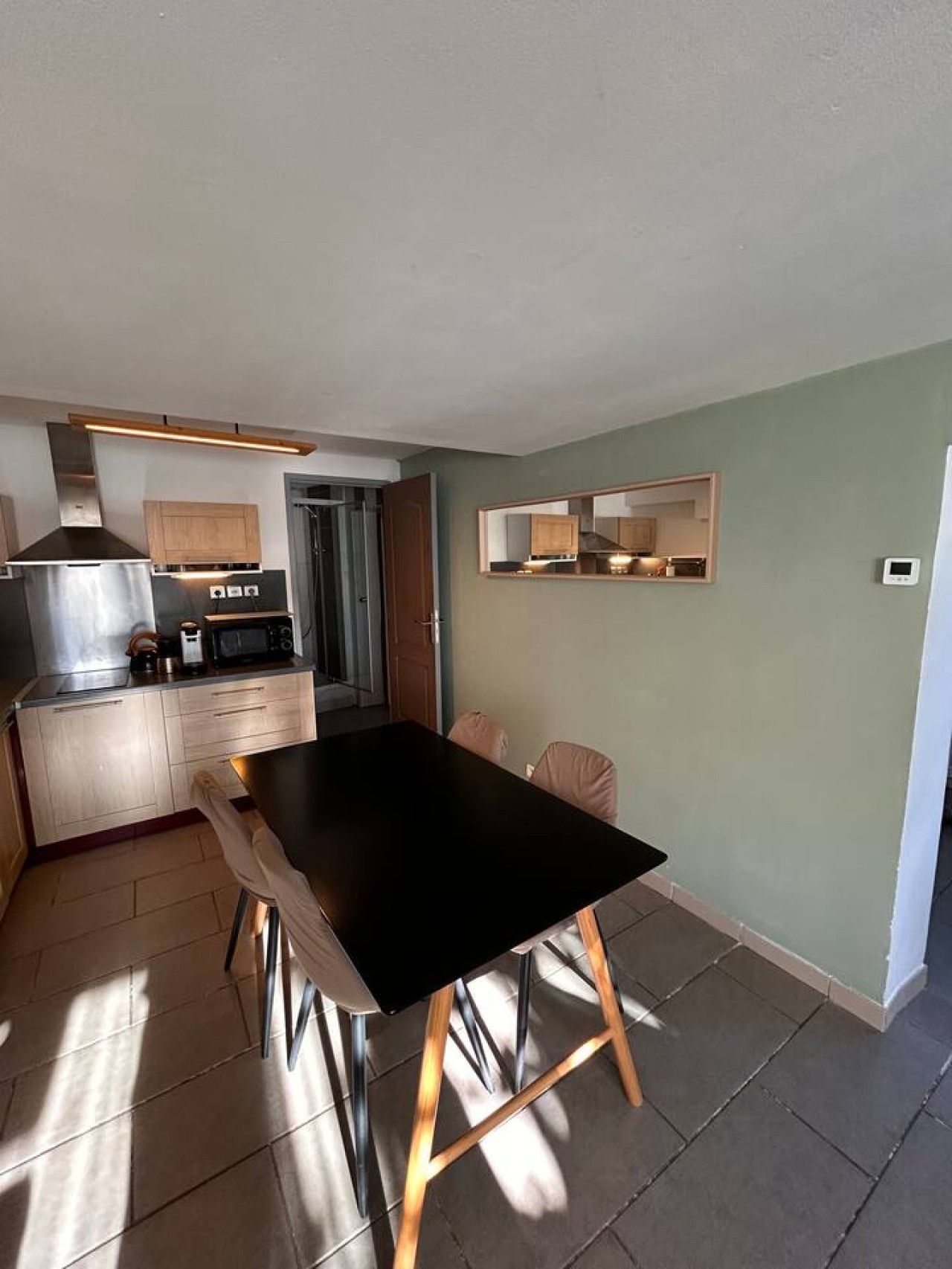 A compact kitchen with modern appliances, a dining area with a black table, and light-colored cabinets.