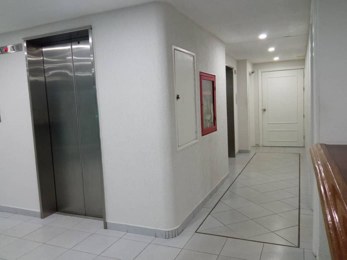 A clean, modern hallway with a metallic elevator, a framed picture on the wall, and a door at the end.