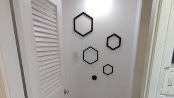 A narrow hallway with white tiled flooring, a door with a louvered window, and a wall with hexagonal wall art.