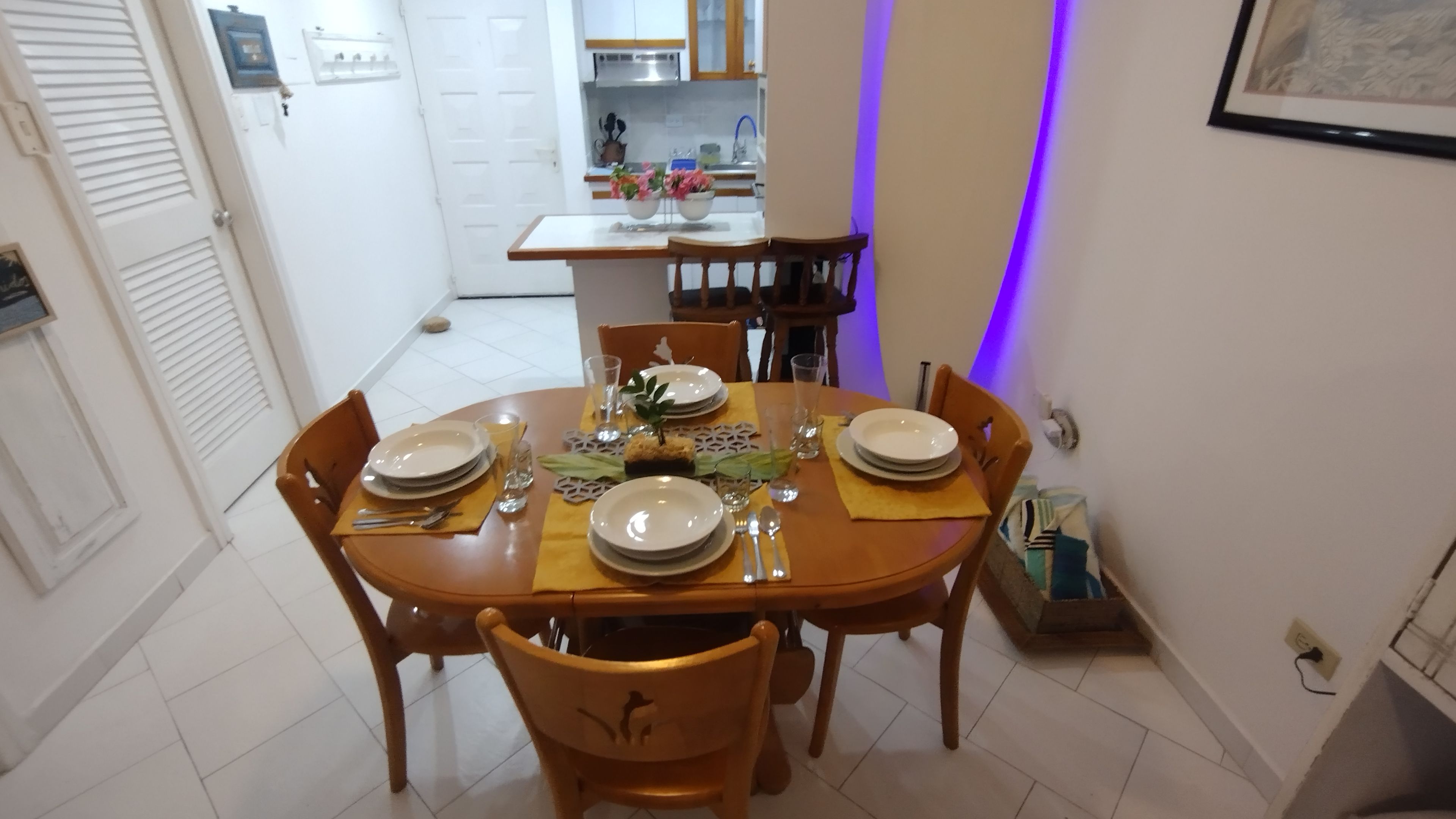 A dining area with a round wooden table set for four, surrounded by chairs.
