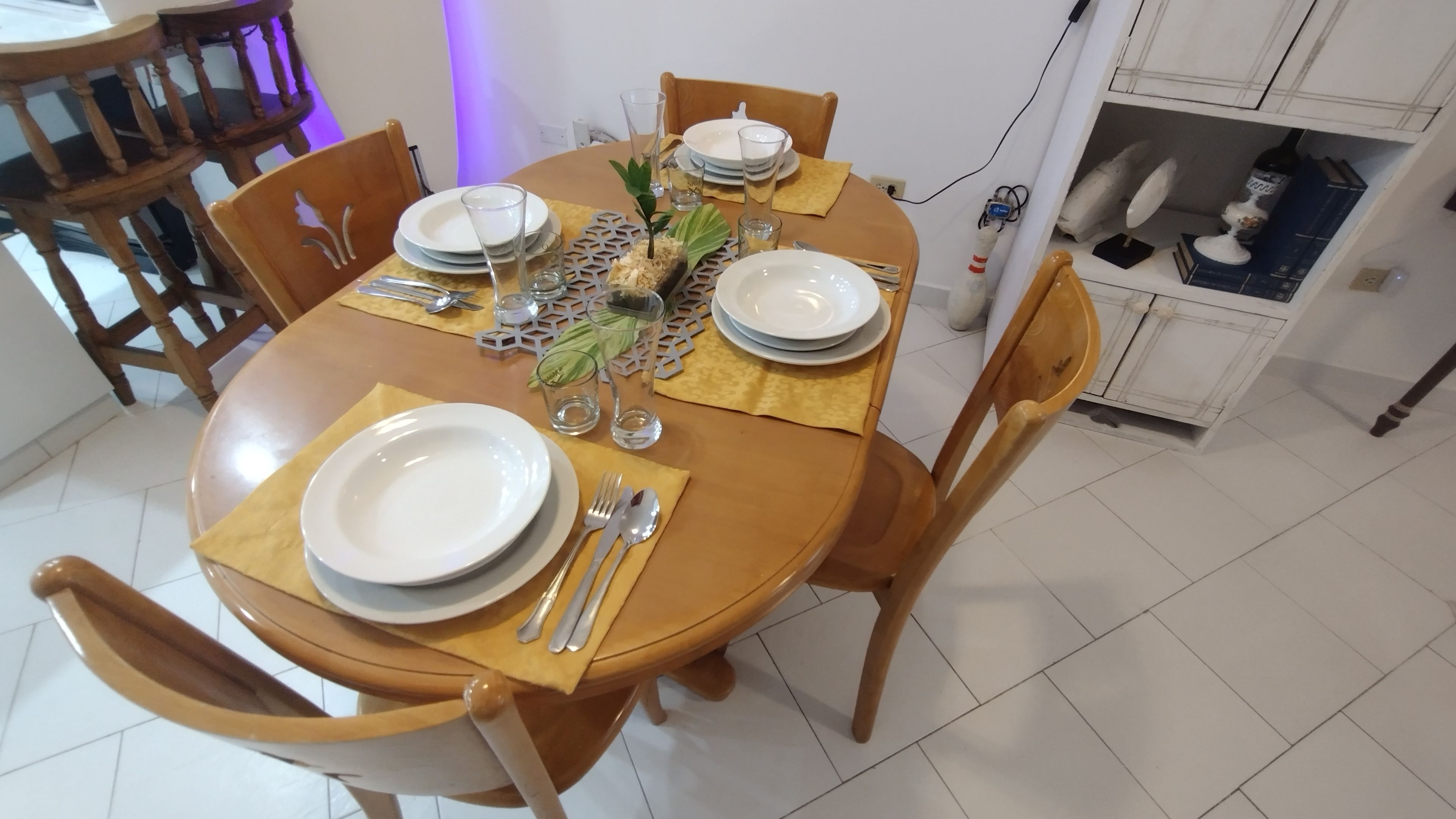 A dining table set with plates, cutlery, and glasses, surrounded by wooden chairs.