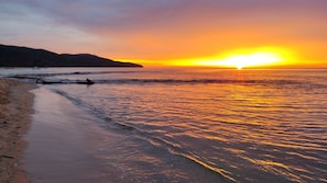 A beach with a sunset, waves, and a distant mountain.