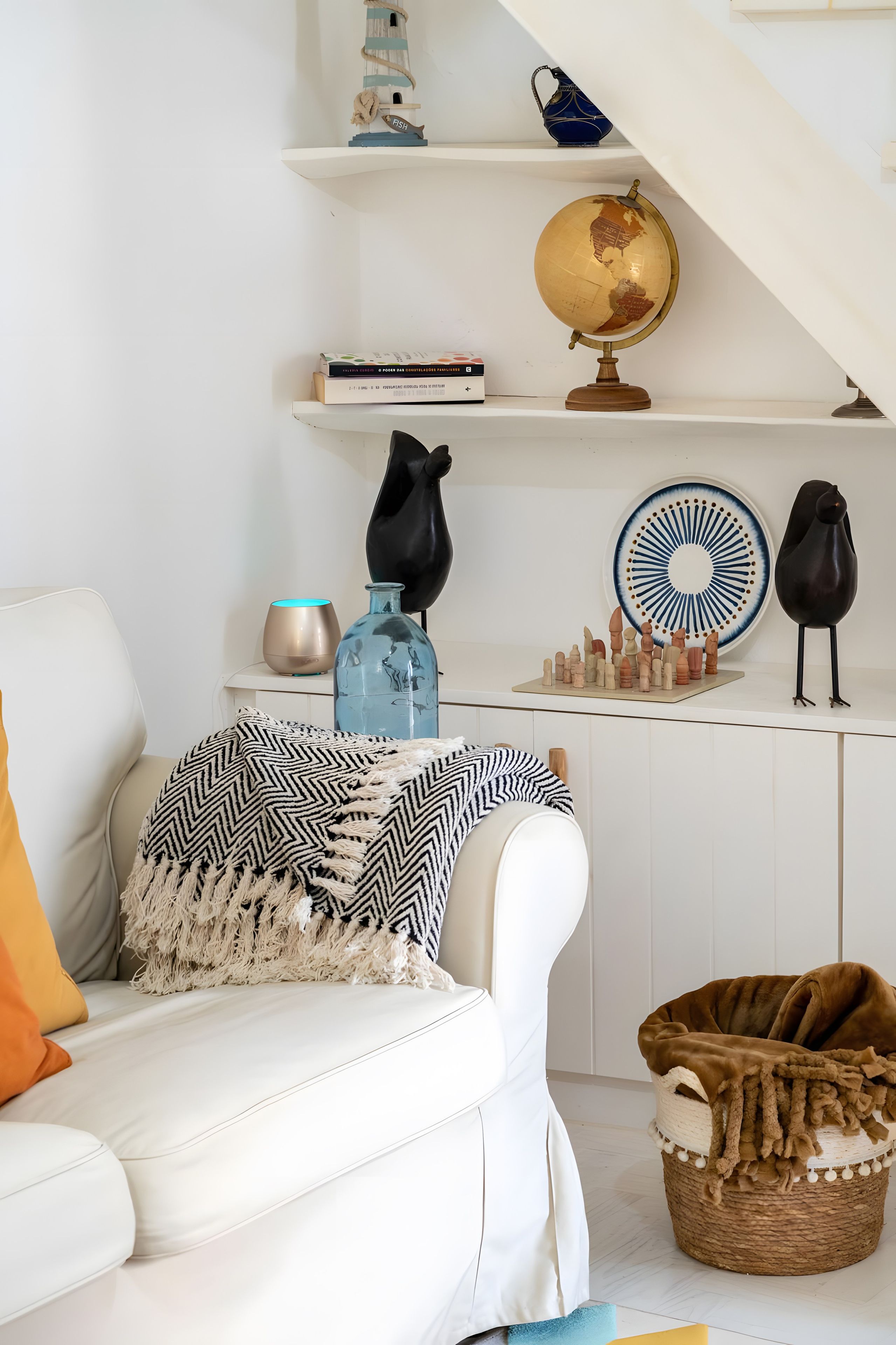 Un salon avec un canapé blanc, un globe terrestre et des objets décoratifs disposés sur des étagères.