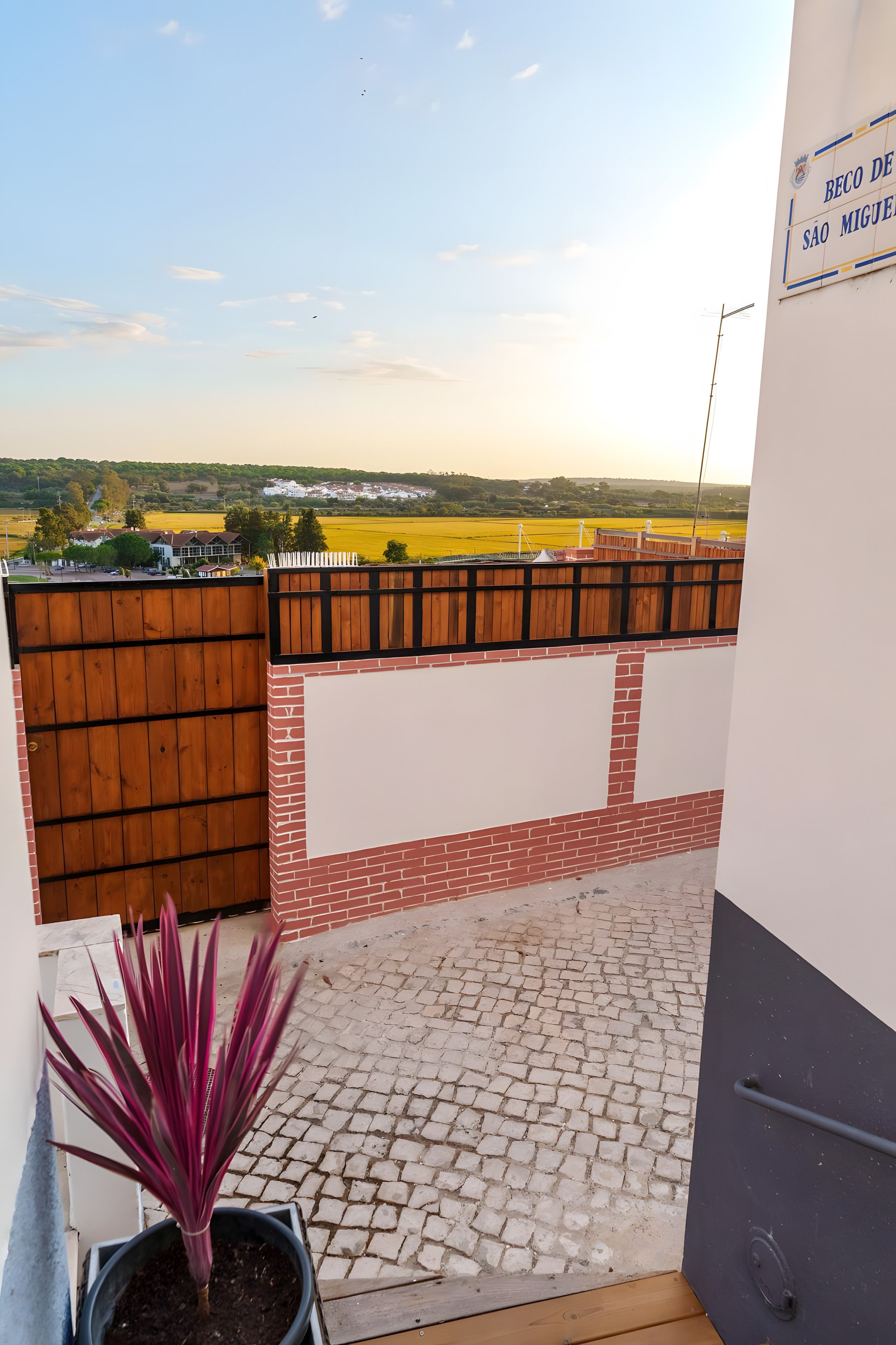 A balcony with a view of a rural landscape, a wooden fence, and a potted plant.