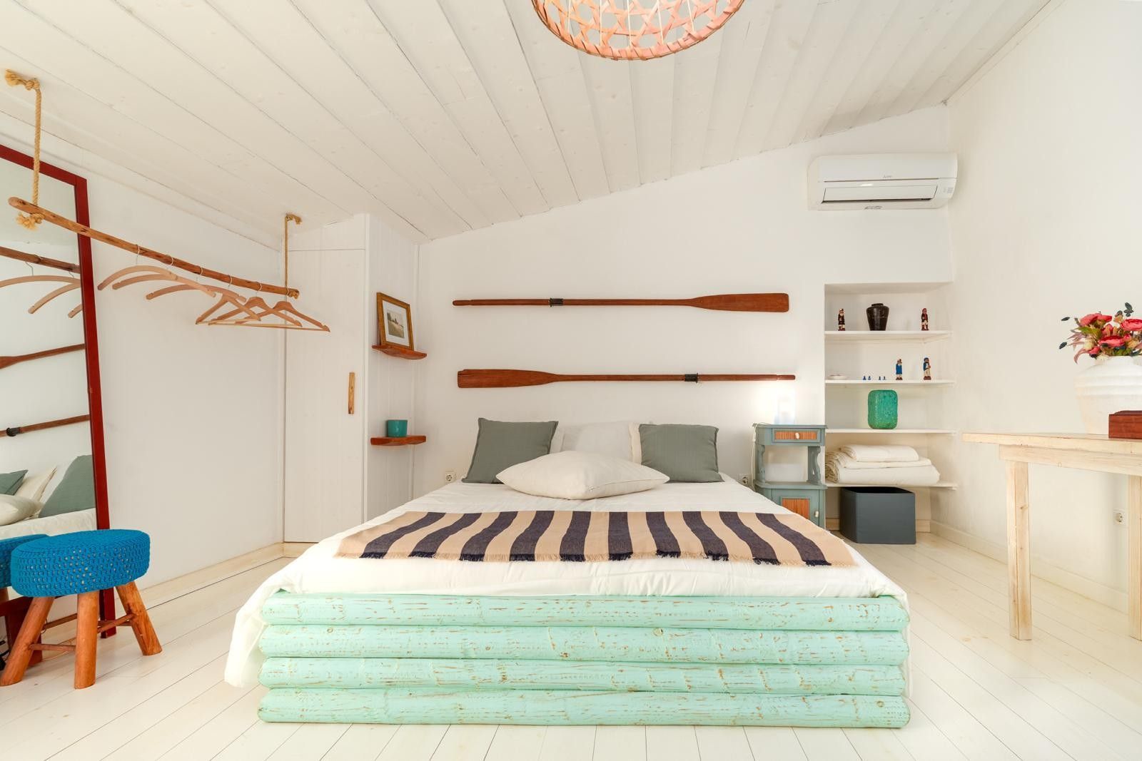 A bedroom with a bed, wooden furniture, a shelf with decorative items, and a hanging wooden paddle.