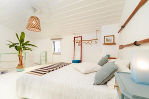 A bedroom with a bed, a hanging plant, a window, and a wooden beam on the ceiling. - Holiday Home 'Cantinho De São Miguel' with Wi-Fi and Air Conditioning (Alcácer do Sal)