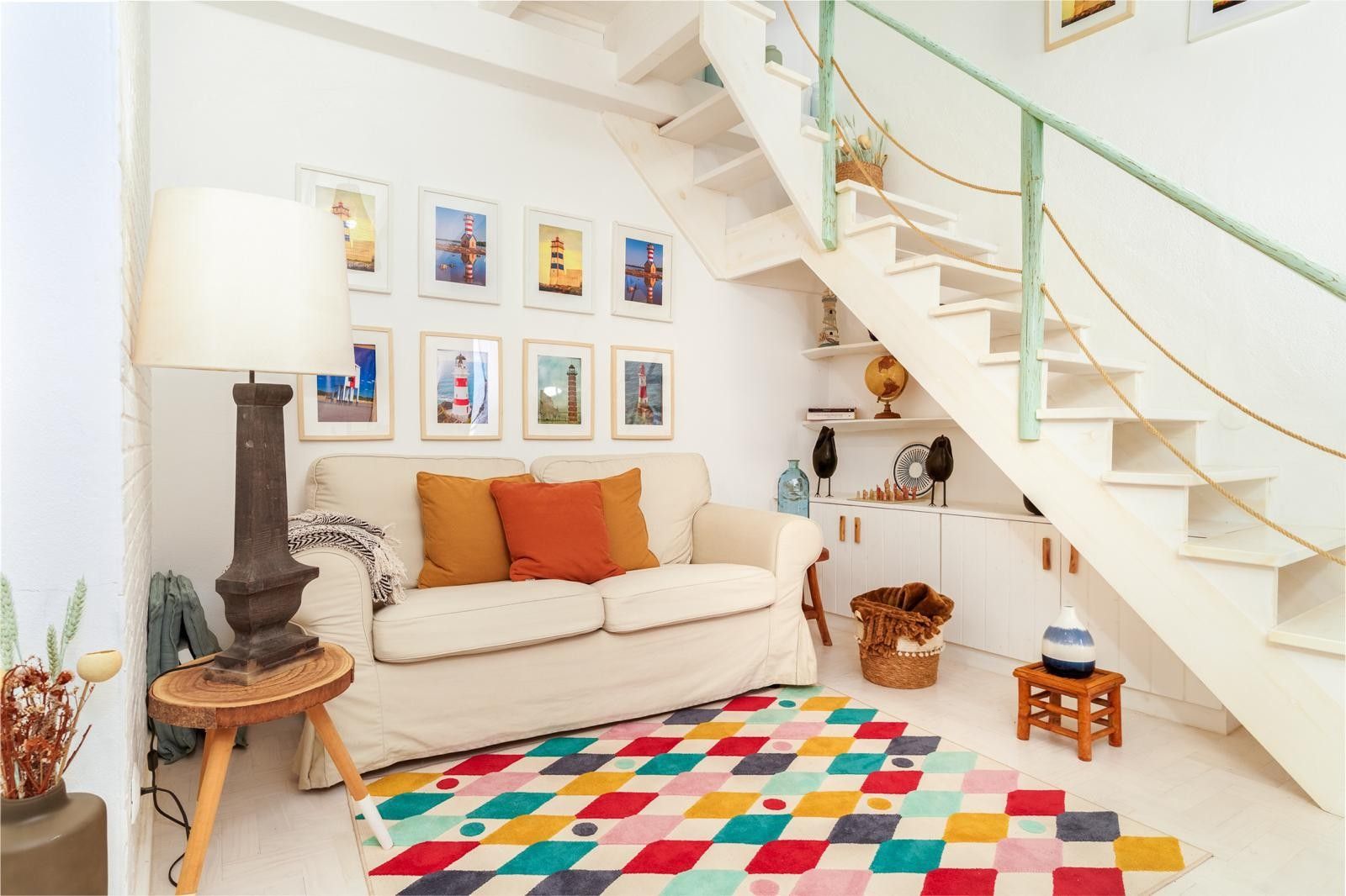 A living room with a staircase, a sofa, a colorful rug, and framed pictures on the wall.