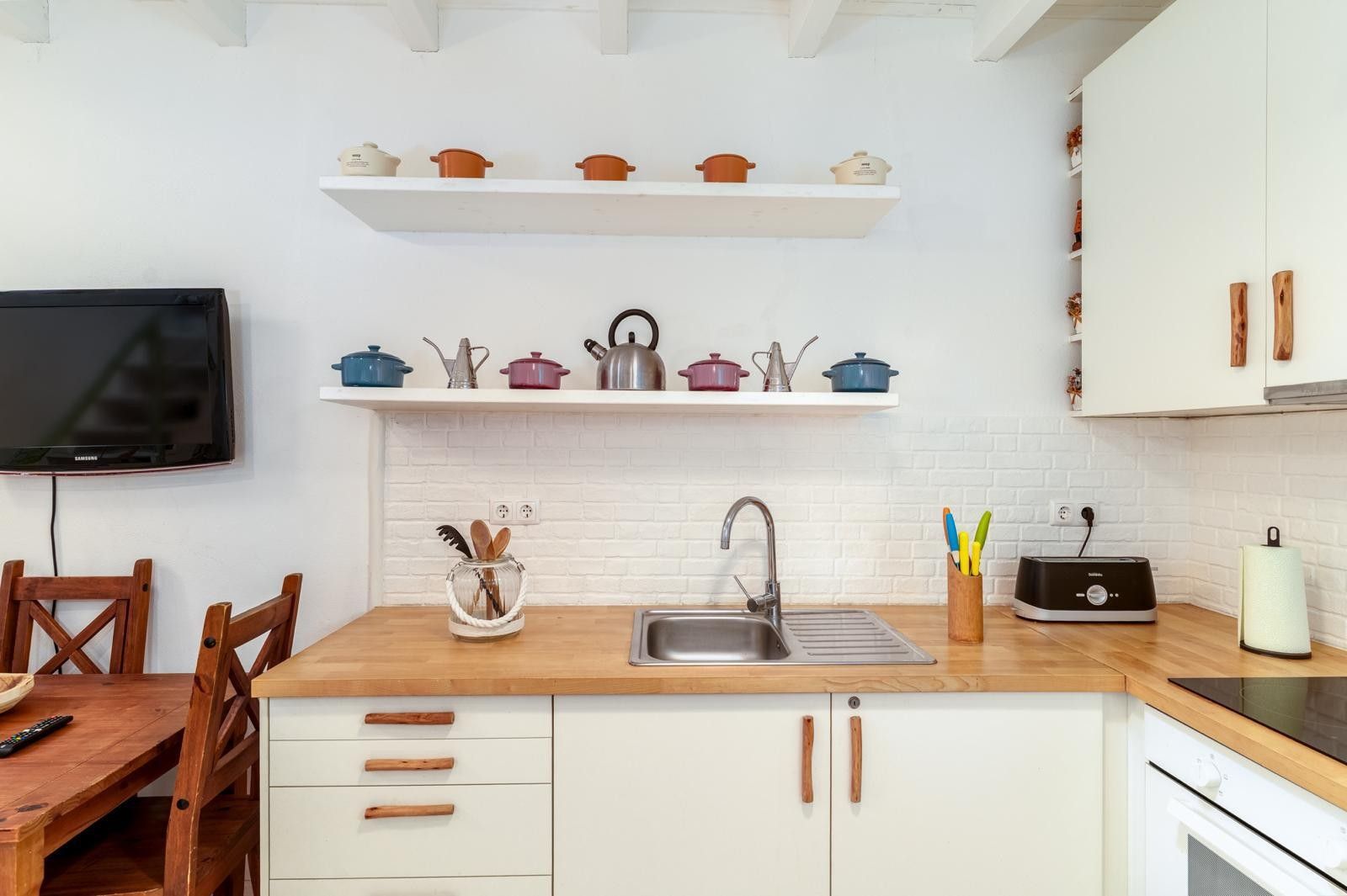 A modern kitchen with white cabinetry, a wooden countertop, a built-in TV, and a variety of kitchen utensils and appliances.