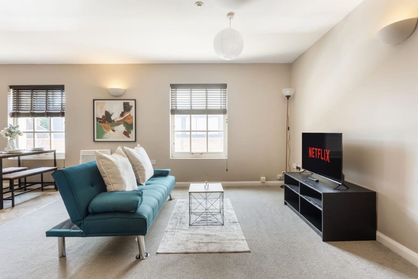 A modern living room with a teal sofa, a coffee table, a flat-screen TV, and a painting on the wall.