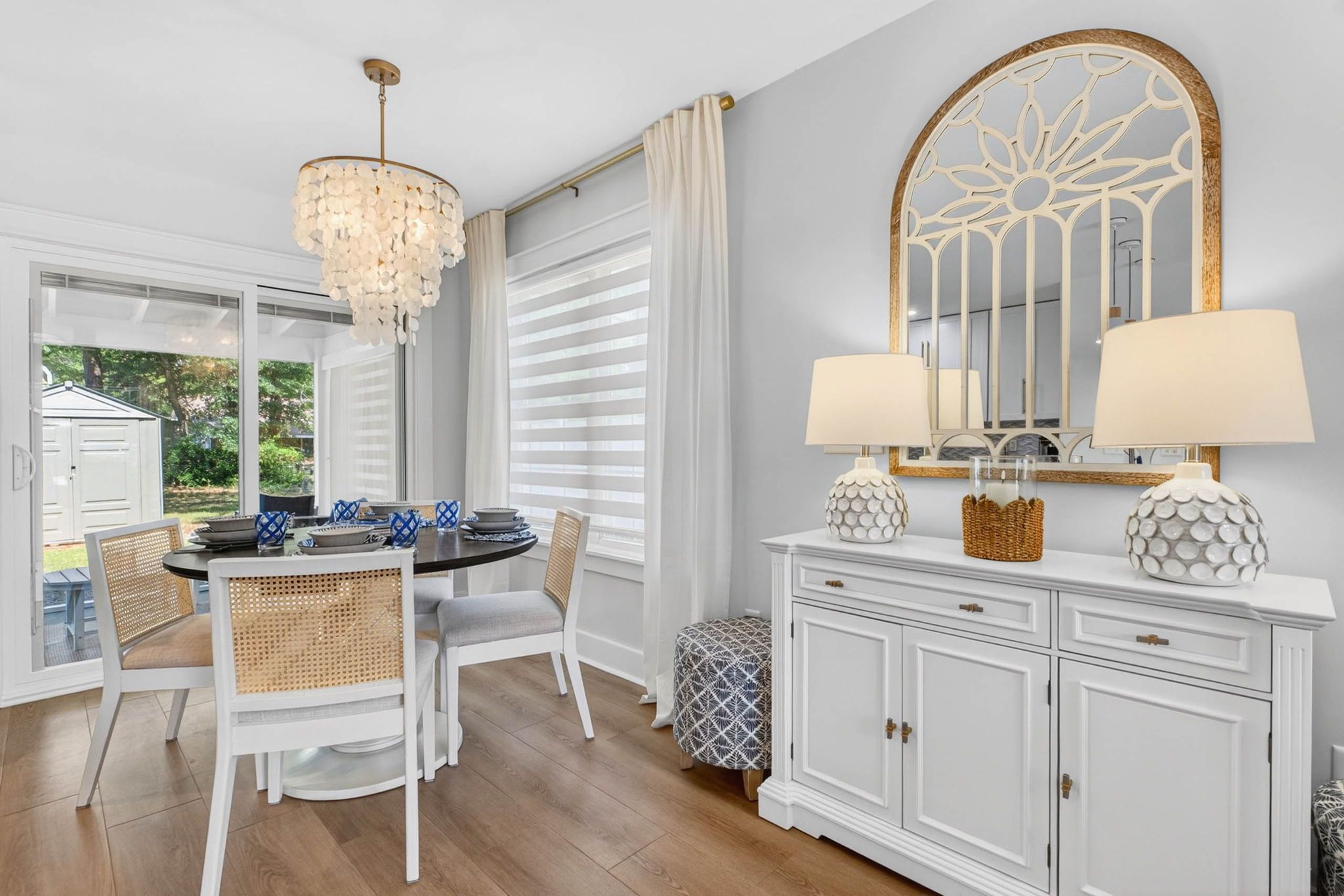 A dining area with a chandelier, white furniture, and a large mirror with a decorative frame.