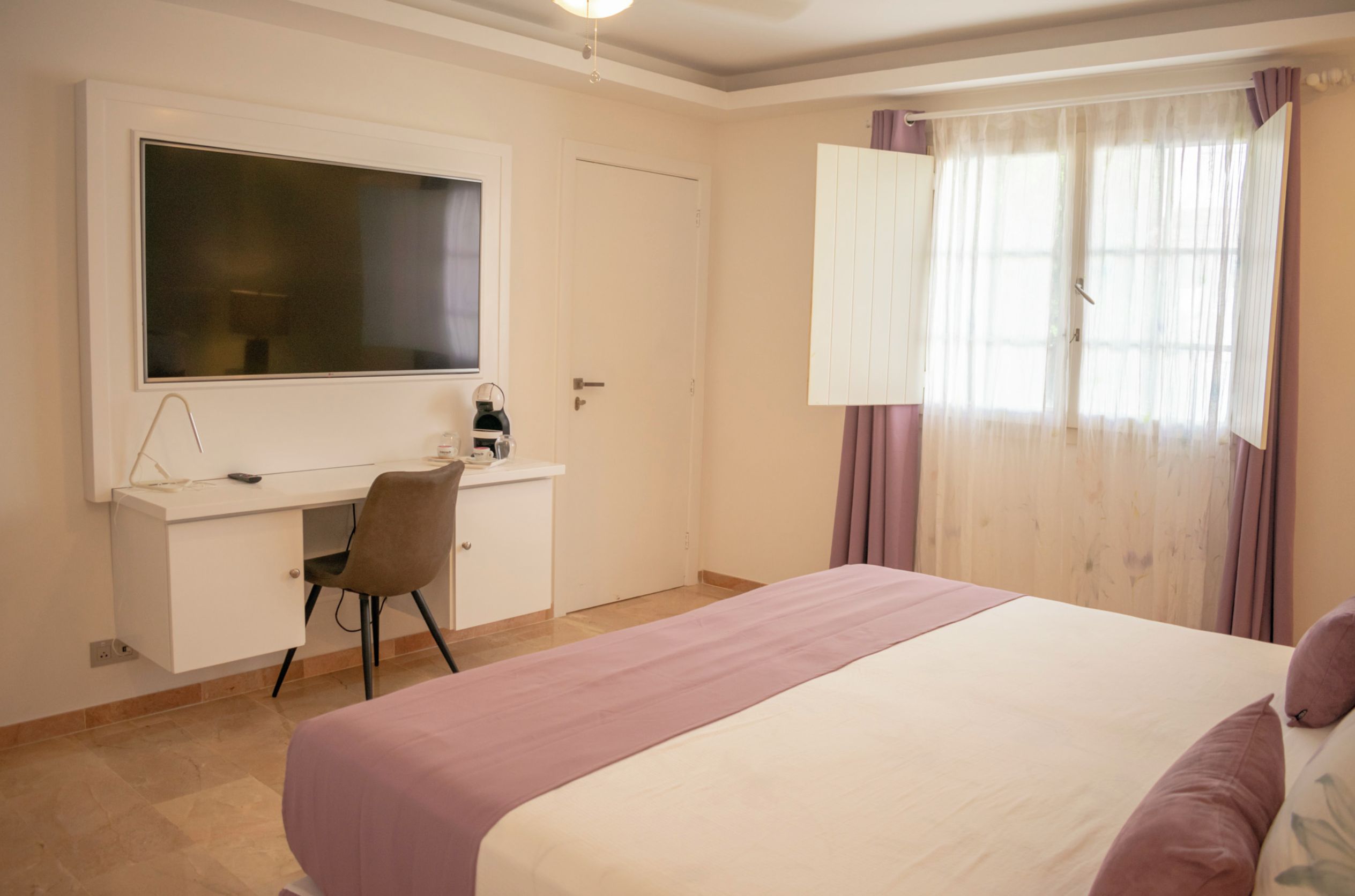 Une chambre à coucher avec un lit, un bureau avec une chaise, une télévision et une fenêtre avec des rideaux.