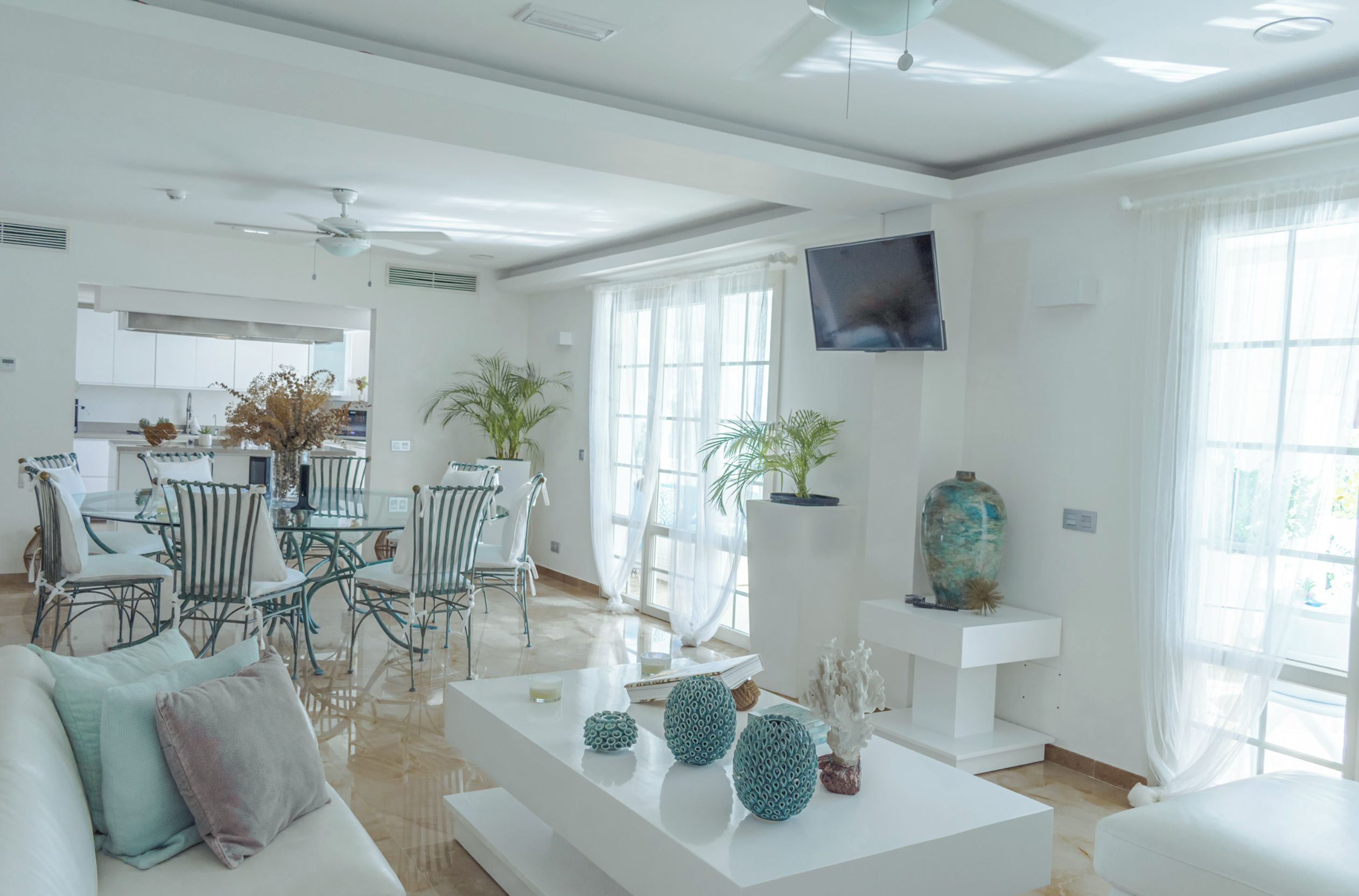 Un salon moderne avec un coin repas, un téléviseur fixé au mur et une cuisine en arrière-plan.