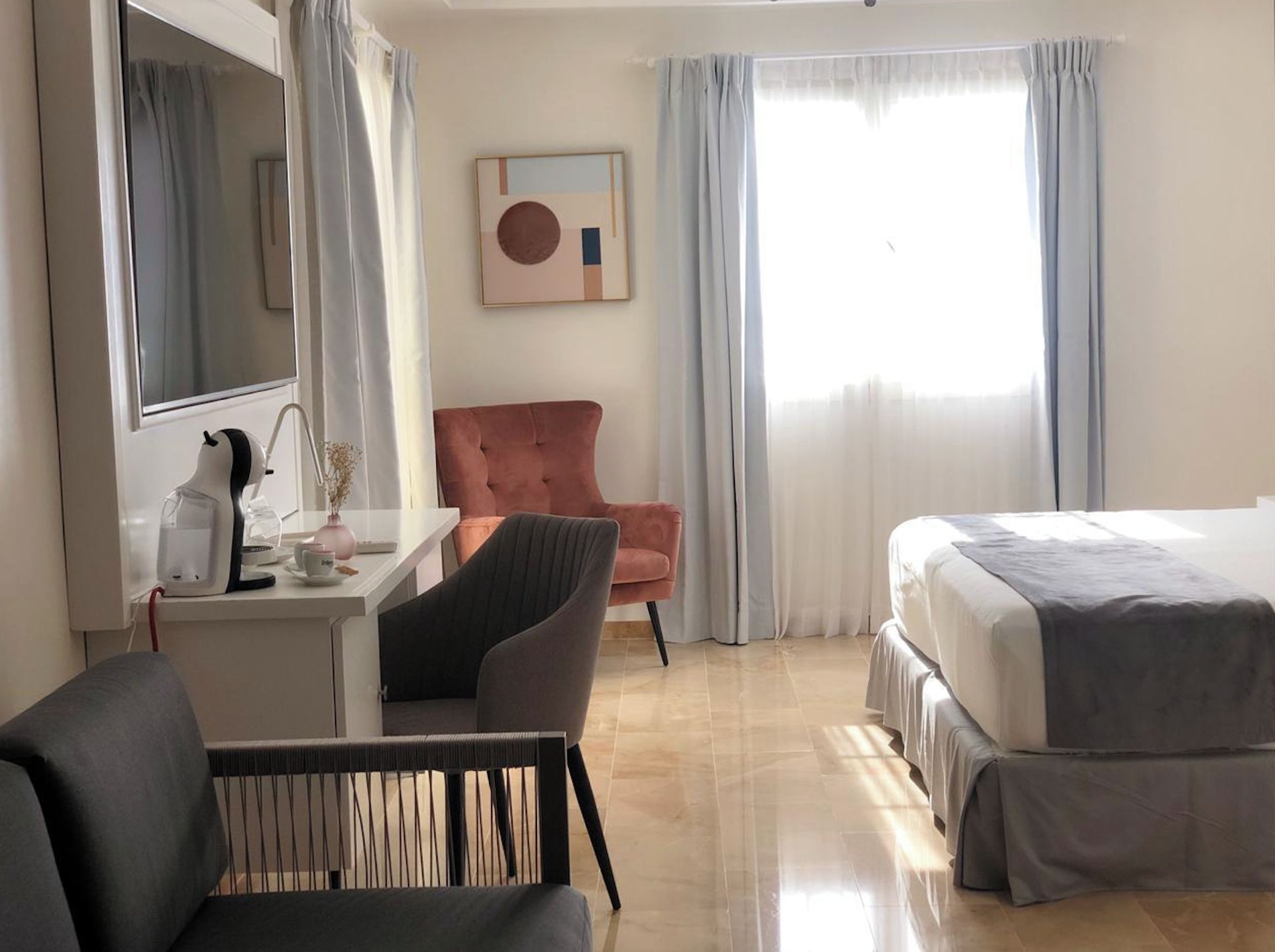 Una habitación de hotel con una cama, un escritorio, una silla y un ventanal con cortinas.