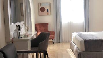 Una habitación de hotel con una cama, un escritorio, una silla y un ventanal con cortinas.