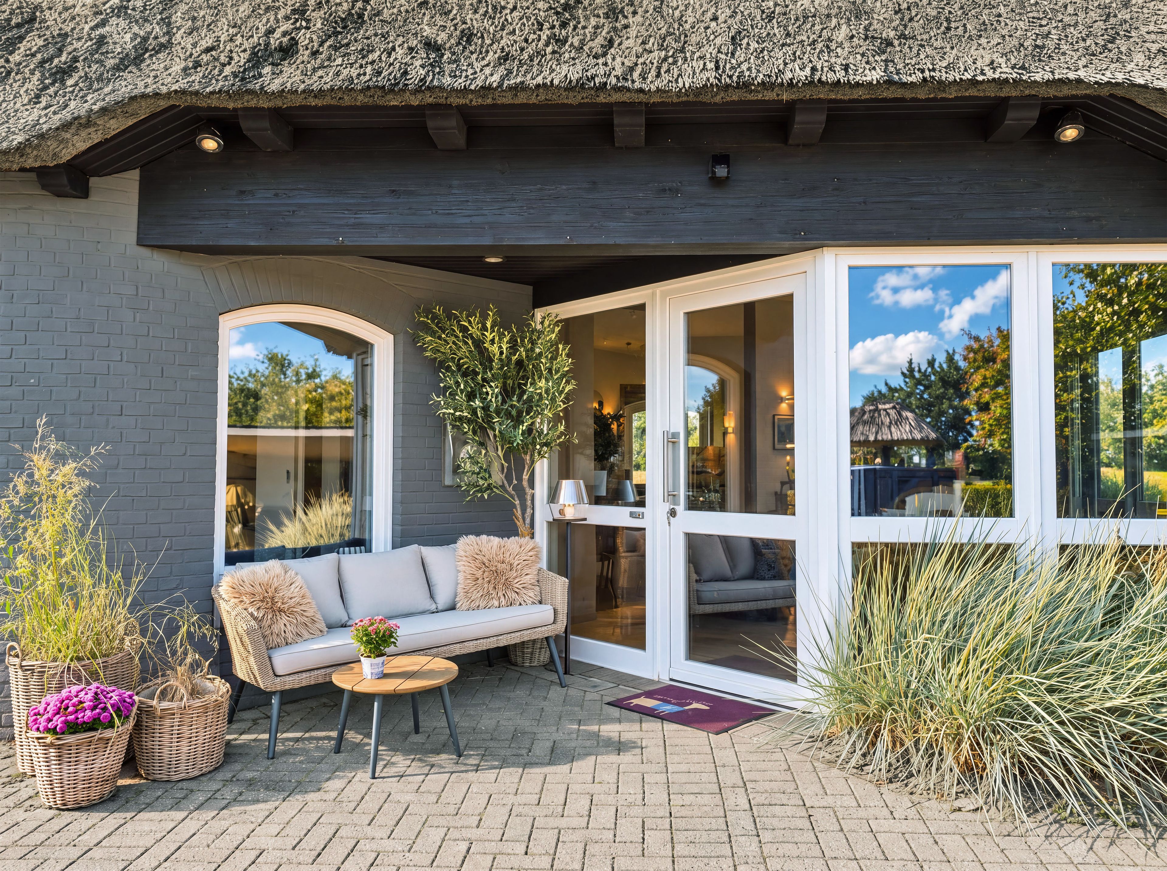 A covered outdoor seating area with a sofa, a small table, and potted plants.