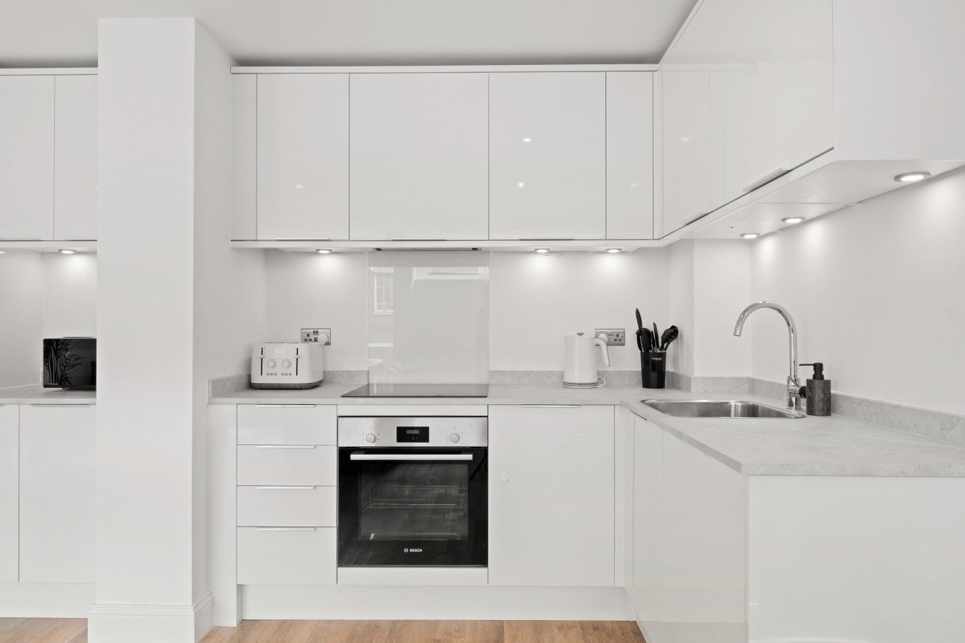 Cozinha moderna com armários brancos, forno Bosch, cafeteira e pia com torneira.